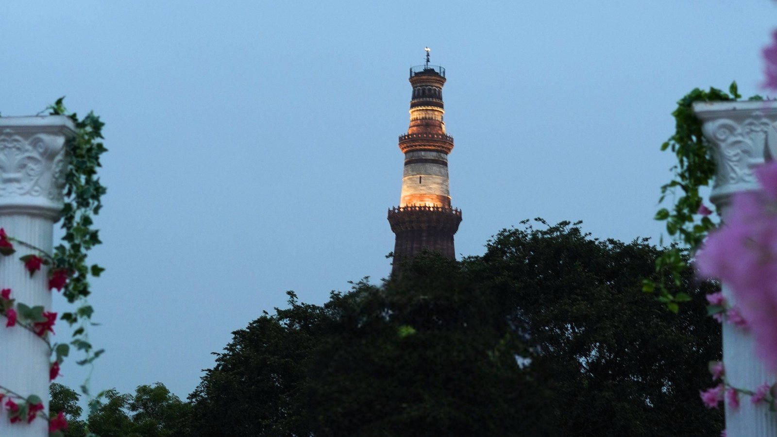 Qutub Minar illuminated at twilight framed by bougainvillea at Alora Delhi